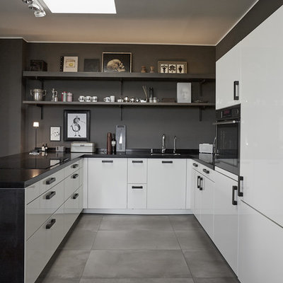 Small trendy u-shaped concrete floor and gray floor open concept kitchen photo in Berlin with a drop-in sink, flat-panel cabinets, white cabinets, brown backsplash, stainless steel appliances, a peninsula and black countertops