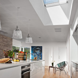 Offene, Zweizeilige Moderne Küche mit integriertem Waschbecken, flächenbündigen Schrankfronten, weißen Schränken, schwarzen Elektrogeräten, braunem Holzboden, Kücheninsel, braunem Boden und weißer Arbeitsplatte in Düsseldorf