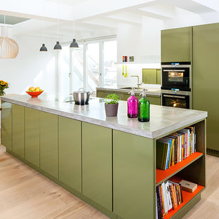 Photo of a large contemporary single-wall open plan kitchen in Berlin with a drop-in sink, flat-panel cabinets, green cabinets, concrete benchtops, white splashback, panelled appliances, light hardwood floors, with island and brown floor.