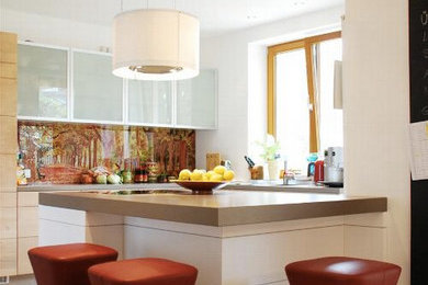 Moderne Küche in U-Form mit flächenbündigen Schrankfronten, hellen Holzschränken, braunem Holzboden, Halbinsel, bunter Rückwand und Glasrückwand in Sonstige