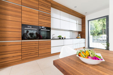 Diseño de cocina lineal contemporánea de tamaño medio abierta sin isla con puertas de armario de madera clara, encimera de granito, salpicadero blanco y electrodomésticos negros