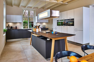 Offene, Geräumige Moderne Küche in L-Form mit flächenbündigen Schrankfronten, schwarzen Elektrogeräten, Keramikboden, Kücheninsel und beigem Boden in Sonstige