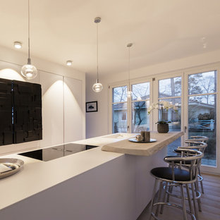 Offene, Zweizeilige, Mittelgroße Moderne Küche mit flächenbündigen Schrankfronten, weißen Schränken, Kücheninsel, schwarzen Elektrogeräten, hellem Holzboden, grauem Boden und weißer Arbeitsplatte in Hamburg