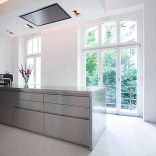 Imagen de cocina lineal, contemporánea, grande, con fregadero de un seno, armarios con paneles lisos, puertas de armario en acero inoxidable, encimera de acero inoxidable, una isla, electrodomésticos negros y suelo de linóleo