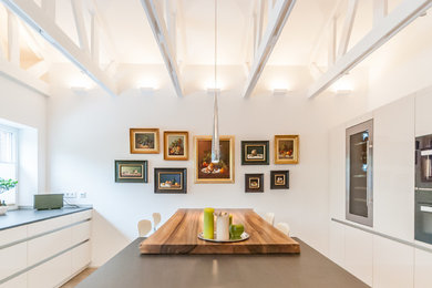 Große Moderne Wohnküche mit flächenbündigen Schrankfronten, weißen Schränken, Kücheninsel und schwarzen Elektrogeräten in Köln