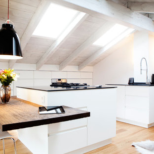 Geschlossene, Große, Zweizeilige Nordische Küche mit flächenbündigen Schrankfronten, weißen Schränken, hellem Holzboden, zwei Kücheninseln, Elektrogeräten mit Frontblende, integriertem Waschbecken, Mineralwerkstoff-Arbeitsplatte, Küchenrückwand in Weiß, Rückwand aus Holz und braunem Boden in München