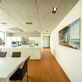 Offene, Zweizeilige, Große Moderne Küche mit flächenbündigen Schrankfronten, weißen Schränken, Laminat-Arbeitsplatte, Küchenrückwand in Weiß, Kücheninsel, weißer Arbeitsplatte, Küchengeräten aus Edelstahl, braunem Holzboden, braunem Boden und Einbauwaschbecken in Stuttgart
