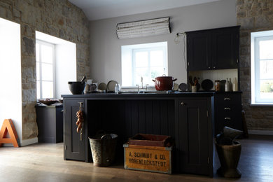 Imagen de cocina de estilo de casa de campo grande abierta con armarios estilo shaker, puertas de armario negras, una isla y encimeras negras