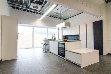 This is an example of an expansive industrial galley open plan kitchen in Frankfurt with an island, flat-panel cabinets, white cabinets, black splashback, grey floors, grey worktops and black appliances.