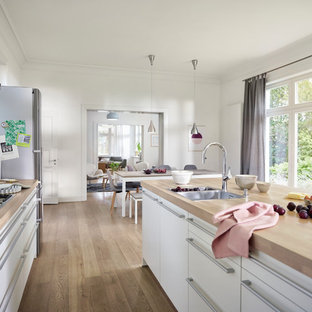Offene, Zweizeilige, Große Nordische Küche mit Einbauwaschbecken, weißen Schränken, Arbeitsplatte aus Holz, Küchenrückwand in Weiß, Glasrückwand, Küchengeräten aus Edelstahl, hellem Holzboden, Kücheninsel, braunem Boden und flächenbündigen Schrankfronten in Hamburg