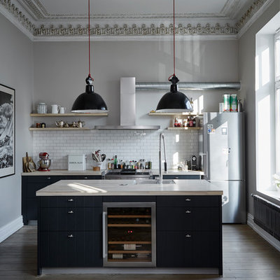 Mid-sized trendy galley brown floor and medium tone wood floor open concept kitchen photo in Hamburg with black cabinets, wood countertops, white backsplash, subway tile backsplash, stainless steel appliances, an island, an undermount sink, flat-panel cabinets and beige countertops