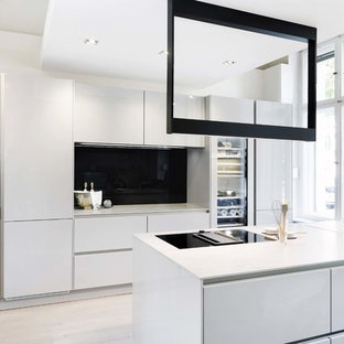 Zweizeilige, Mittelgroße Moderne Küche mit Einbauwaschbecken, flächenbündigen Schrankfronten, weißen Schränken, Küchenrückwand in Schwarz, Glasrückwand, schwarzen Elektrogeräten, hellem Holzboden, Halbinsel, beigem Boden und weißer Arbeitsplatte in Berlin