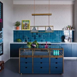 Photo of a small eclectic single-wall kitchen in Berlin with flat-panel cabinets, blue cabinets, glass benchtops, blue splashback, concrete floors, with island and window splashback.