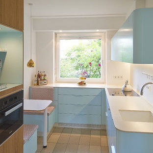 Geschlossene, Kleine Moderne Küche ohne Insel in U-Form mit integriertem Waschbecken, flächenbündigen Schrankfronten, blauen Schränken, Küchenrückwand in Weiß, schwarzen Elektrogeräten, beigem Boden und weißer Arbeitsplatte in Köln