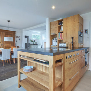 Offene, Geräumige Landhaus Küche mit flächenbündigen Schrankfronten, hellbraunen Holzschränken, Halbinsel, schwarzer Arbeitsplatte, Unterbauwaschbecken, Marmor-Arbeitsplatte, Küchenrückwand in Blau, Rückwand aus Steinfliesen, Küchengeräten aus Edelstahl, Betonboden und grauem Boden in Düsseldorf