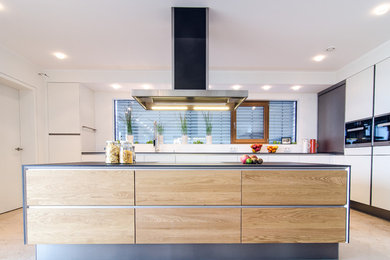Imagen de cocinas en L actual de tamaño medio abierta con una isla, armarios con paneles lisos, electrodomésticos negros, suelo de madera clara y suelo beige