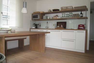 Idéer för ett litet modernt linjärt kök med öppen planlösning, med släta luckor, vita skåp, träbänkskiva, vitt stänkskydd, glaspanel som stänkskydd, mellanmörkt trägolv och brunt golv