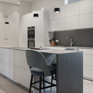 Mittelgroße Moderne Küche mit flächenbündigen Schrankfronten, weißen Schränken, Küchenrückwand in Grau, schwarzen Elektrogeräten, hellem Holzboden, Kücheninsel, beigem Boden und grauer Arbeitsplatte in Berlin