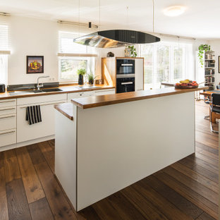 Moderne Wohnküche in L-Form mit Unterbauwaschbecken, flächenbündigen Schrankfronten, weißen Schränken, Arbeitsplatte aus Holz, dunklem Holzboden, Kücheninsel, braunem Boden und brauner Arbeitsplatte in Sonstige