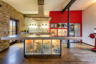 Modern inredning av ett mycket stort kök, med en integrerad diskho, luckor med glaspanel, bänkskiva i rostfritt stål, vitt stänkskydd, rostfria vitvaror, mellanmörkt trägolv och en köksö