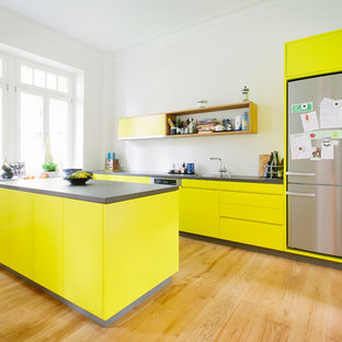 Offene, Zweizeilige Moderne Küche mit Einbauwaschbecken, flächenbündigen Schrankfronten, gelben Schränken, Küchenrückwand in Weiß, Küchengeräten aus Edelstahl, braunem Holzboden, zwei Kücheninseln und braunem Boden in Köln