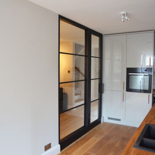 Inspiration for a small traditional l-shaped open plan kitchen in London with a drop-in sink, flat-panel cabinets, grey cabinets, wood benchtops, white splashback, subway tile splashback, black appliances, light hardwood floors, no island, brown floor, brown benchtop and wallpaper.