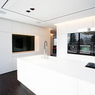 Idées déco pour une très grand cuisine ouverte moderne avec un évier intégré, un placard à porte plane, des portes de placard blanches, une crédence noire, une crédence en feuille de verre, un électroménager noir, un sol en bois foncé et un îlot central.