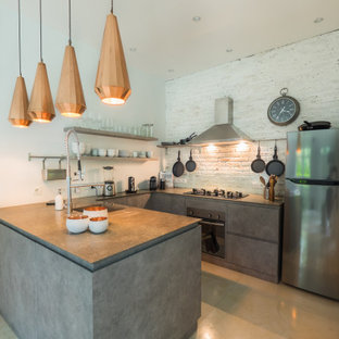 This is an example of a small mediterranean u-shaped open plan kitchen with a drop-in sink, flat-panel cabinets, grey cabinets, marble benchtops, white splashback, brick splashback, stainless steel appliances, concrete floors, with island, beige floor and grey benchtop.