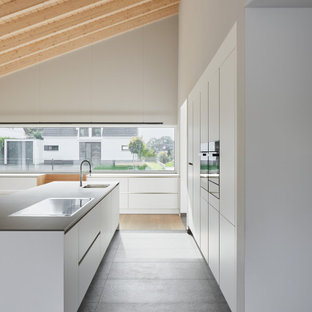Modelo de cocina comedor lineal, moderna, con fregadero encastrado, armarios con paneles lisos, puertas de armario blancas, encimera de granito, salpicadero blanco, salpicadero de madera, electrodomésticos de acero inoxidable, suelo de terrazo, una isla, suelo gris y encimeras grises