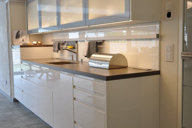 Modelo de cocina actual de tamaño medio con fregadero integrado, armarios con paneles lisos, puertas de armario blancas, salpicadero blanco, salpicadero de vidrio templado y suelo gris
