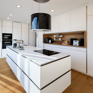 Esempio di una cucina minimal di medie dimensioni con lavello integrato, ante lisce, ante bianche, top in superficie solida, paraspruzzi bianco, paraspruzzi in legno, elettrodomestici neri, pavimento in legno verniciato e pavimento marrone