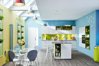 Große Moderne Wohnküche mit flächenbündigen Schrankfronten, weißen Schränken, Küchenrückwand in Grün, Kücheninsel, braunem Holzboden und schwarzen Elektrogeräten in Hamburg