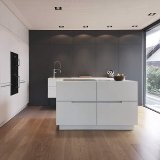 Zweizeilige, Mittelgroße Moderne Küche mit Kücheninsel, Unterbauwaschbecken, flächenbündigen Schrankfronten, grauen Schränken, Elektrogeräten mit Frontblende, braunem Holzboden, braunem Boden und weißer Arbeitsplatte in Sonstige