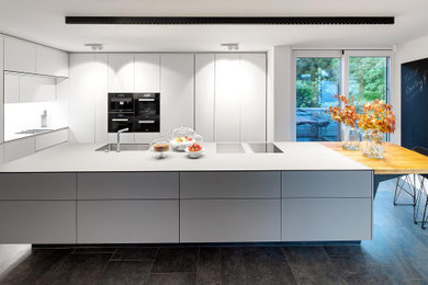 Große Moderne Wohnküche mit flächenbündigen Schrankfronten, weißen Schränken, Kücheninsel, grauer Arbeitsplatte und schwarzem Boden in Stuttgart