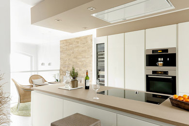 На фото: кухня-гостиная среднего размера в современном стиле с плоскими фасадами, белыми фасадами, техникой под мебельный фасад и островом