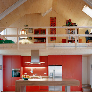 Offene, Einzeilige, Große Moderne Küche mit flächenbündigen Schrankfronten, Arbeitsplatte aus Holz, Küchenrückwand in Orange, Küchengeräten aus Edelstahl, braunem Holzboden, Kücheninsel und roten Schränken in München