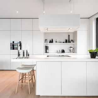 Offene, Einzeilige Moderne Küche mit flächenbündigen Schrankfronten, weißen Schränken, Mineralwerkstoff-Arbeitsplatte, Küchenrückwand in Weiß, hellem Holzboden, Kücheninsel, weißer Arbeitsplatte, Waschbecken und beigem Boden in Hamburg