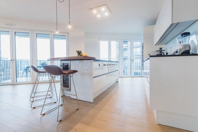 Offene, Zweizeilige, Mittelgroße Moderne Küche mit weißen Schränken, Granit-Arbeitsplatte, braunem Holzboden, Kücheninsel, braunem Boden und schwarzer Arbeitsplatte in Frankfurt am Main