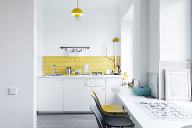 На фото: прямая кухня в скандинавском стиле с одинарной мойкой, плоскими фасадами, белыми фасадами, желтым фартуком, фартуком из плитки кабанчик и темным паркетным полом без острова