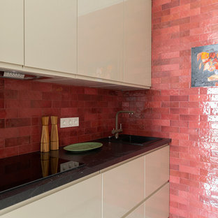 Diseño de cocina de galera, clásica renovada, pequeña, cerrada, sin isla, con fregadero de un seno, armarios con paneles lisos, puertas de armario beige, encimera de laminado, salpicadero rojo, salpicadero de azulejos tipo metro, electrodomésticos de acero inoxidable, suelo de baldosas de porcelana, suelo blanco y encimeras negras