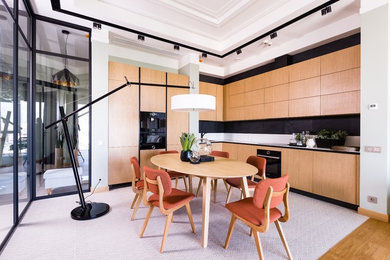 Источник вдохновения для домашнего уюта: угловая кухня-гостиная в современном стиле с плоскими фасадами, светлыми деревянными фасадами, черным фартуком и белым полом без острова