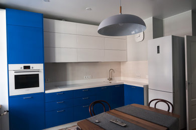 На фото: угловая кухня в скандинавском стиле с обеденным столом, плоскими фасадами, синими фасадами, столешницей из акрилового камня, бежевым фартуком и белой столешницей