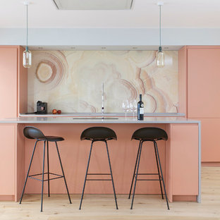 Offene, Zweizeilige, Große Moderne Küche mit flächenbündigen Schrankfronten, orangefarbenen Schränken, Mineralwerkstoff-Arbeitsplatte, Küchenrückwand in Gelb, Rückwand aus Marmor, Küchengeräten aus Edelstahl, Kücheninsel, hellem Holzboden und beigem Boden in Barcelona