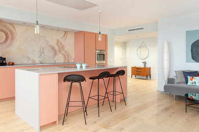 На фото: параллельная кухня-гостиная среднего размера в современном стиле с плоскими фасадами, розовым фартуком, техникой из нержавеющей стали, светлым паркетным полом, островом и бежевым полом с
