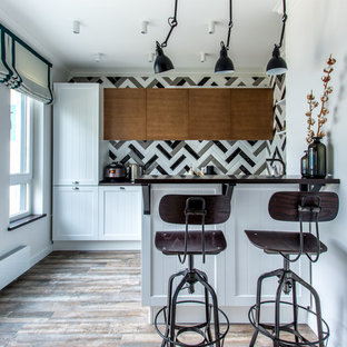 Modelo de cocina blanca y negra, clásica renovada, con armarios con paneles empotrados, salpicadero multicolor, suelo marrón y península