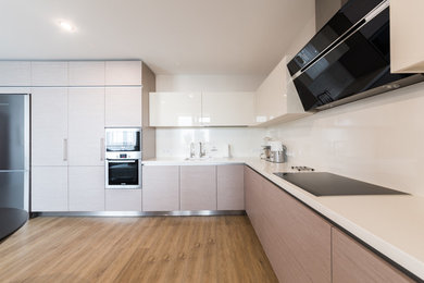 Modelo de cocinas en L contemporánea con armarios con paneles lisos, puertas de armario de madera clara, salpicadero blanco, electrodomésticos de acero inoxidable y suelo de madera en tonos medios