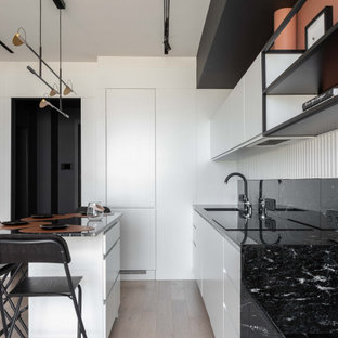 This is an example of a small scandinavian single-wall eat-in kitchen in Moscow with an undermount sink, flat-panel cabinets, white cabinets, granite benchtops, black splashback, granite splashback, black appliances, light hardwood floors, with island, grey floor and black benchtop.