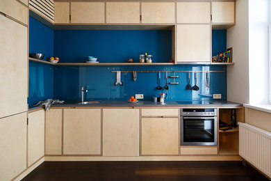 サンクトペテルブルクにある北欧スタイルのおしゃれなL型キッチン (フラットパネル扉のキャビネット、コンクリートカウンター、青いキッチンパネル、ガラス板のキッチンパネル、シルバーの調理設備、濃色無垢フローリング、アイランドなし、茶色い床、グレーのキッチンカウンター、淡色木目調キャビネット) の写真