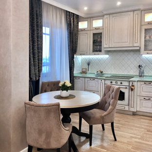 Photo of a transitional l-shaped eat-in kitchen with an integrated sink, glass-front cabinets, beige cabinets, solid surface benchtops, white splashback, ceramic splashback, panelled appliances, light hardwood floors, no island and turquoise benchtop.