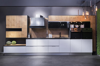 На фото: отдельная, прямая кухня среднего размера в современном стиле с плоскими фасадами и светлыми деревянными фасадами